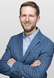 Headshot of Ben Marchionna smiling with his arms crossed wearing a plaid suit jacket and a collard shirt