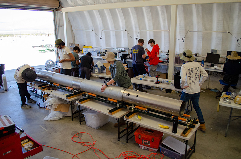 A group of people from MASA rockets standing in a warehouse assembling their rocket.