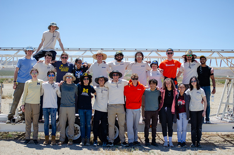 The MASA rocket team standing and smiling for a group picture in front of the rocket launch rail in the middle of the desert.