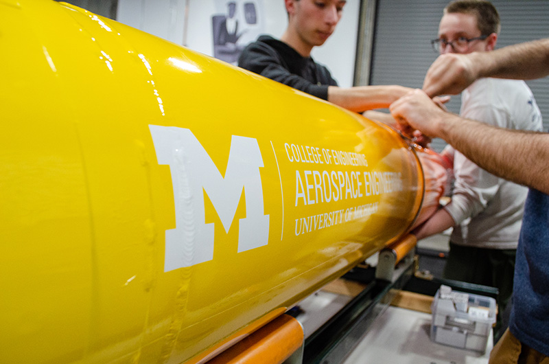 Close up of the MASA rocket with the "College of Engineering Aerospace Engineering at the University of Michigan" logo on the side.